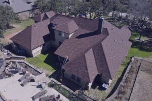 Aerial drone view of a large residential home with a brown shingle roof, used to inspect for common signs you need a new roof like granule loss or wind damage.