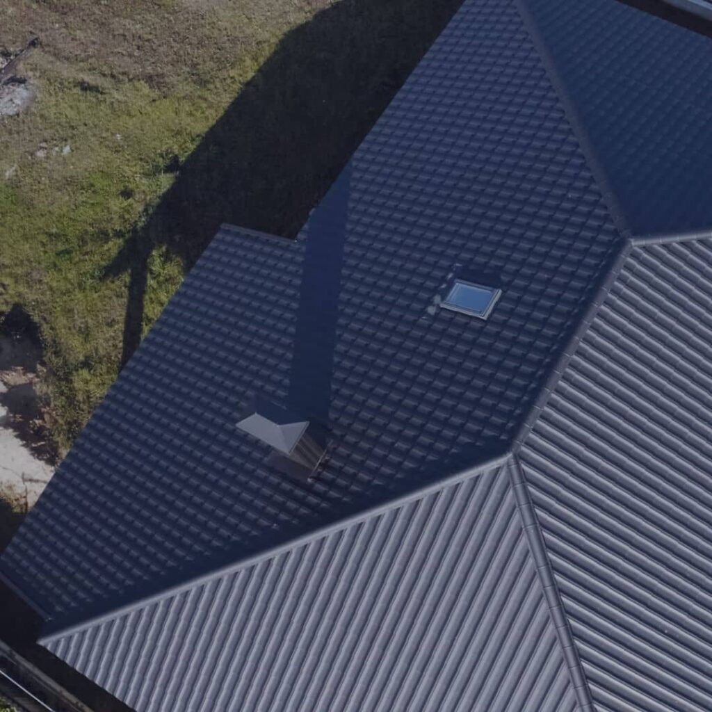 Aerial view of a dark metal tile roof and lighter ribbed metal roof on the same home