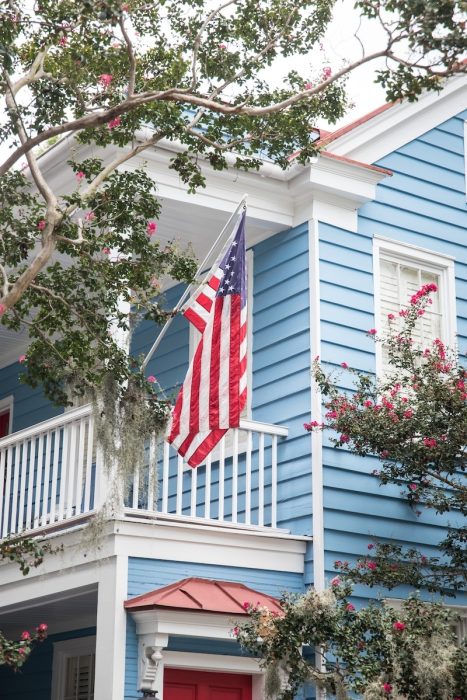 Exterior view of a light blue two-story coastal home with an American flag on the balcony, representing a typical property evaluated during a home inspection in Destin, FL.